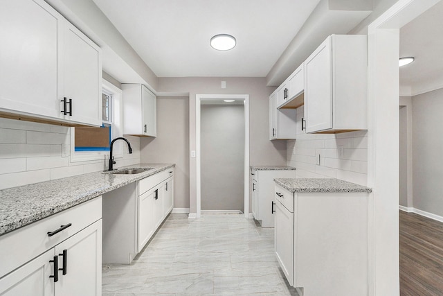 kitchen featuring tasteful backsplash, light stone countertops, sink, and white cabinets