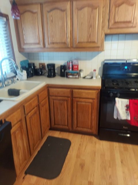 kitchen featuring sink, black range oven, light wood-type flooring, decorative backsplash, and dishwashing machine