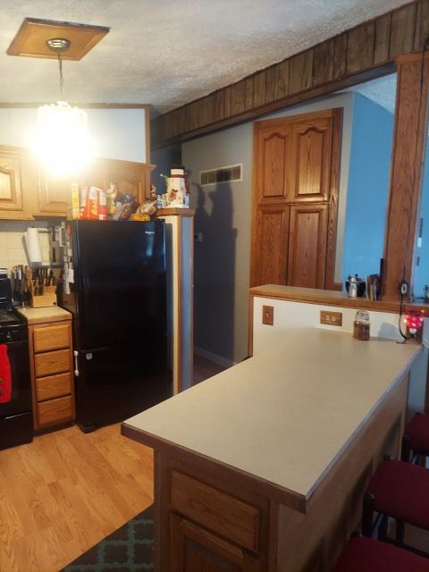 kitchen featuring a textured ceiling, light wood-type flooring, tasteful backsplash, kitchen peninsula, and black appliances