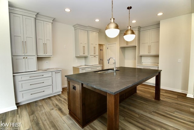kitchen with a sink, dark wood-type flooring, a center island with sink, recessed lighting, and baseboards