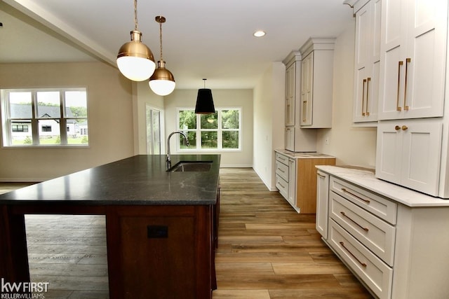 kitchen featuring a sink, recessed lighting, wood finished floors, dark stone counters, and pendant lighting