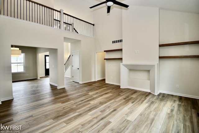 unfurnished living room featuring ceiling fan, wood finished floors, stairway, a towering ceiling, and baseboards