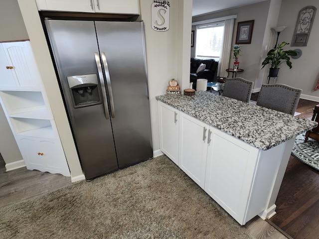 kitchen with white cabinets, light stone counters, kitchen peninsula, and stainless steel refrigerator with ice dispenser