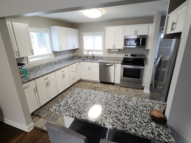 kitchen with white cabinetry, sink, light stone counters, wood-type flooring, and appliances with stainless steel finishes