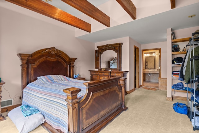 bedroom with connected bathroom, beamed ceiling, and light colored carpet