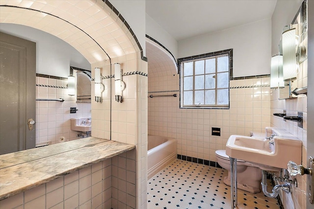 bathroom featuring sink, a bath, toilet, and tile walls