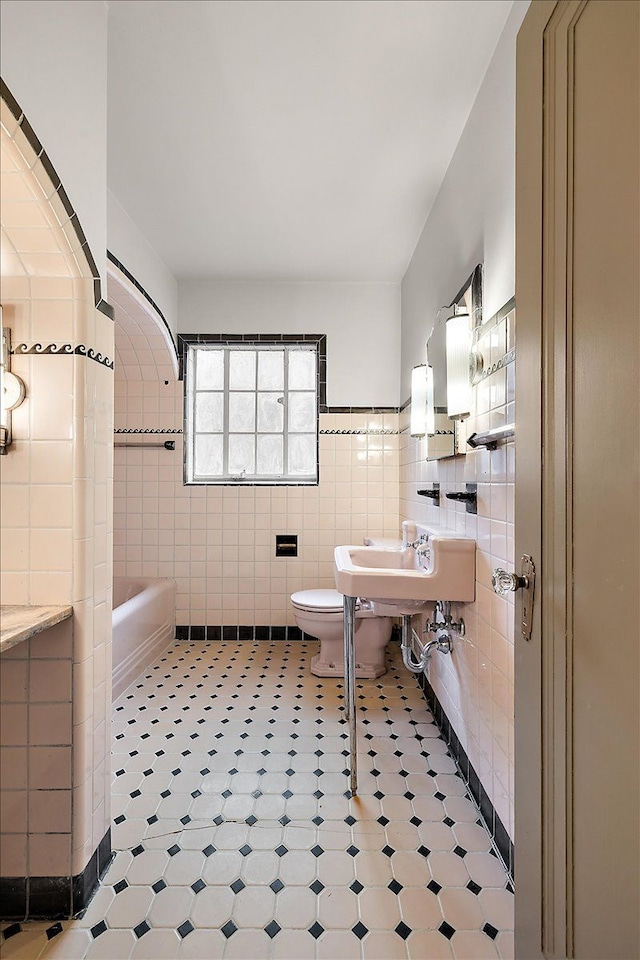 bathroom featuring a washtub, tile patterned flooring, tile walls, and toilet