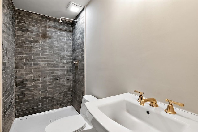 bathroom featuring tiled shower, toilet, and sink