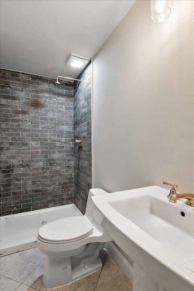 bathroom with tile patterned floors, sink, a tile shower, and toilet