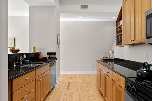 kitchen with dark stone countertops, sink, stainless steel appliances, and light wood-type flooring