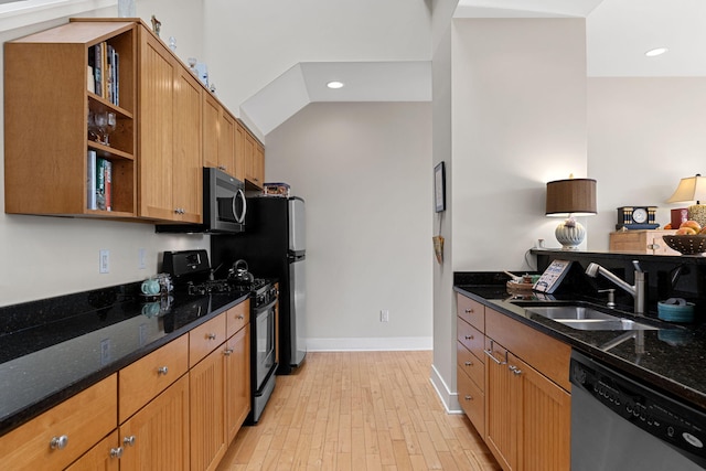 kitchen featuring appliances with stainless steel finishes, sink, light hardwood / wood-style flooring, and dark stone countertops