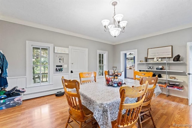 dining room featuring baseboard heating, light hardwood / wood-style flooring, ornamental molding, and a notable chandelier