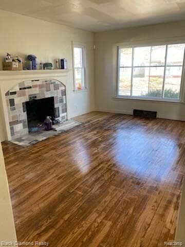 unfurnished living room with a tiled fireplace and wood-type flooring