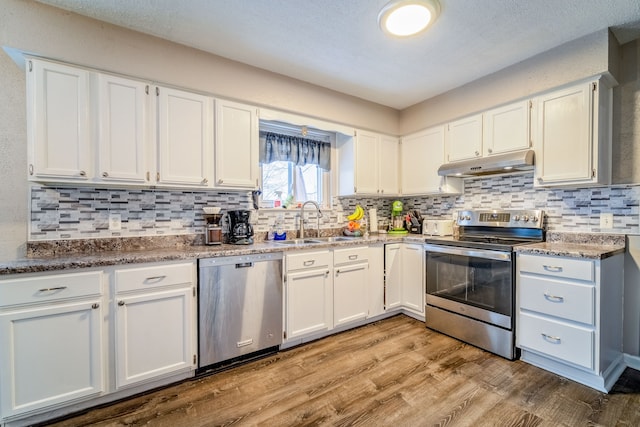 kitchen with backsplash, white cabinets, sink, light wood-type flooring, and appliances with stainless steel finishes