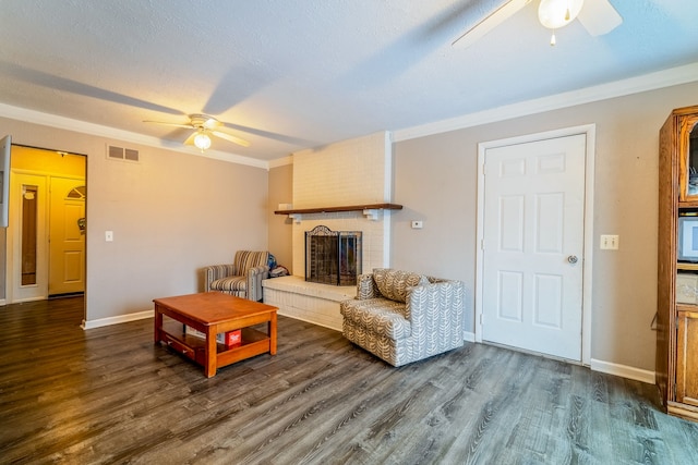 living room with a brick fireplace, a textured ceiling, crown molding, and dark wood-type flooring