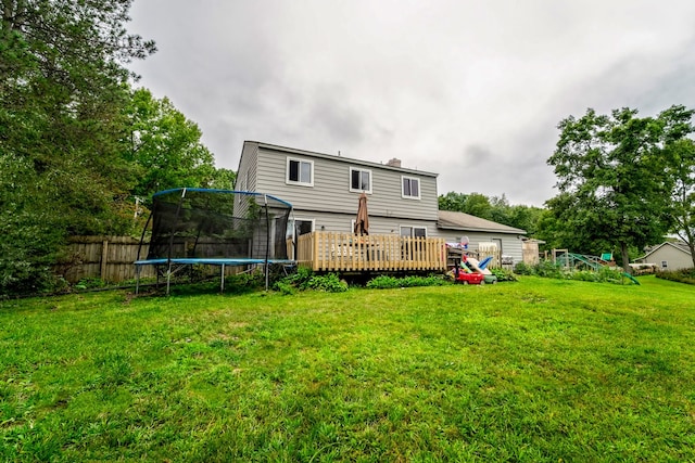 rear view of house with a trampoline, a deck, and a lawn