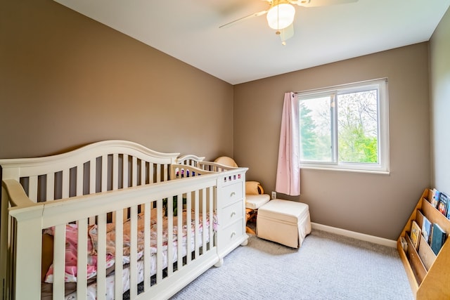 carpeted bedroom featuring ceiling fan and a nursery area