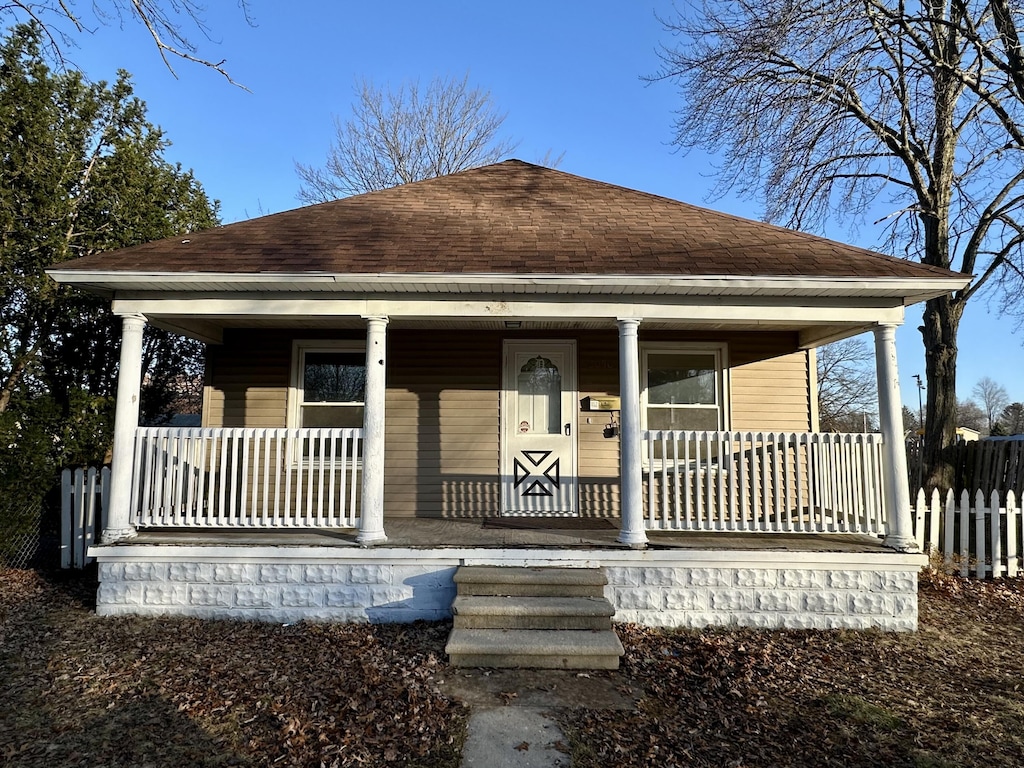 bungalow-style house featuring fence, covered porch, and a shingled roof