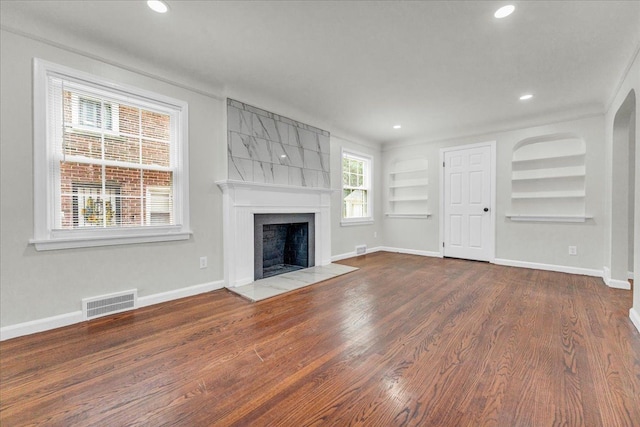 unfurnished living room with built in shelves, crown molding, a tile fireplace, and hardwood / wood-style flooring