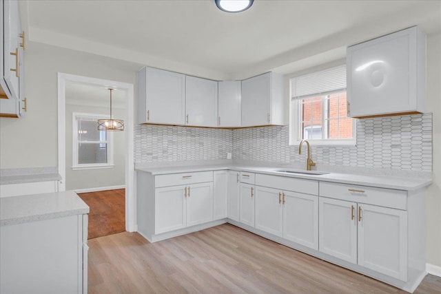 kitchen with backsplash, sink, decorative light fixtures, light hardwood / wood-style flooring, and white cabinetry