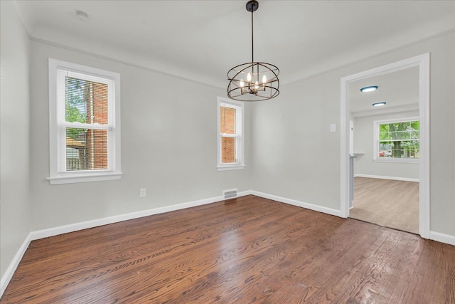 empty room with a chandelier, ornamental molding, and dark wood-type flooring