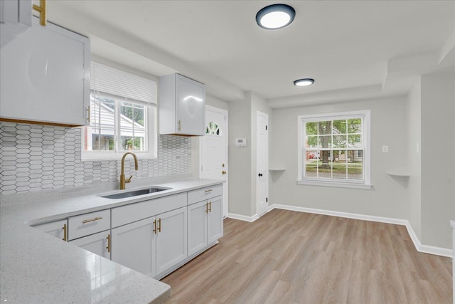 kitchen featuring tasteful backsplash, white cabinetry, sink, and light stone counters