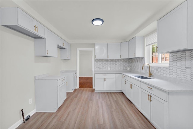 kitchen with light hardwood / wood-style flooring, white cabinetry, tasteful backsplash, and sink