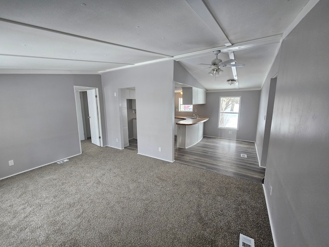 unfurnished living room with dark colored carpet, vaulted ceiling, and ceiling fan