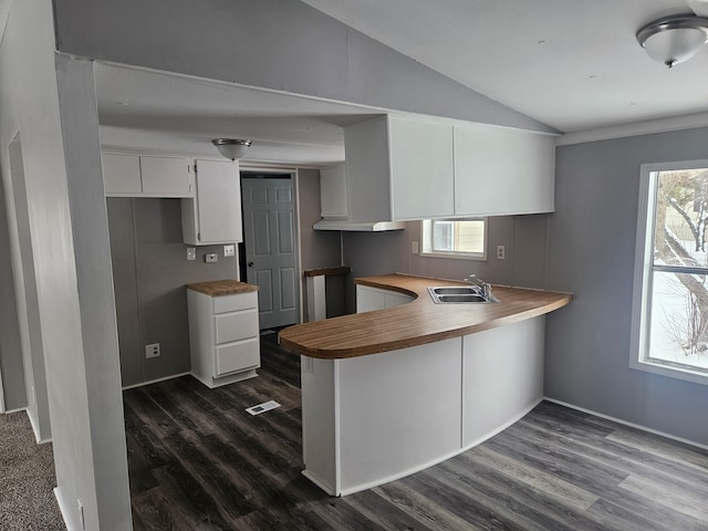 kitchen with sink, dark hardwood / wood-style flooring, kitchen peninsula, lofted ceiling, and white cabinets