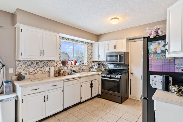 kitchen with appliances with stainless steel finishes, light tile patterned floors, tasteful backsplash, and white cabinetry