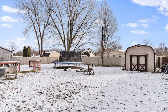 yard covered in snow featuring central AC unit, a storage shed, a trampoline, and a wooden deck