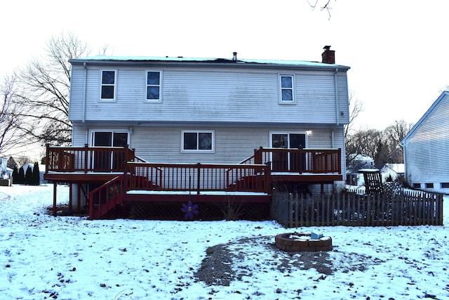 snow covered back of property featuring an outdoor fire pit, a chimney, and a wooden deck