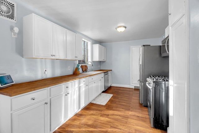 kitchen featuring white cabinets, sink, light hardwood / wood-style flooring, appliances with stainless steel finishes, and butcher block counters