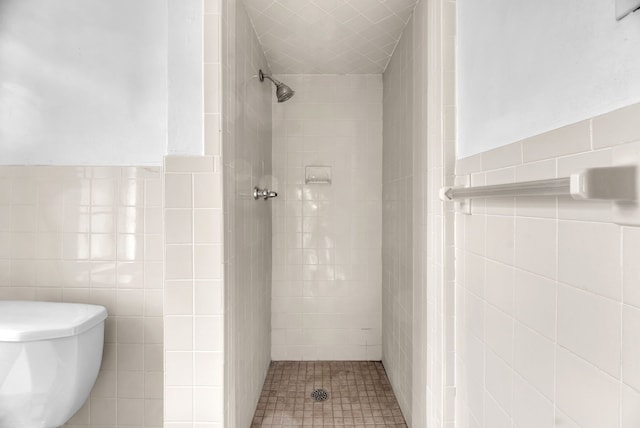 bathroom with toilet, a tile shower, and tile walls