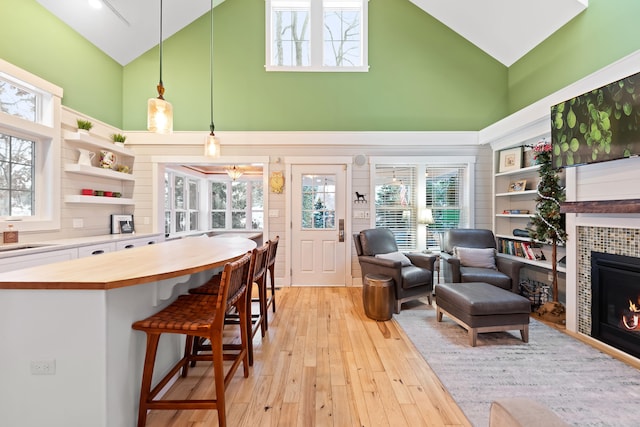 kitchen featuring high vaulted ceiling, pendant lighting, light hardwood / wood-style floors, a breakfast bar area, and a tiled fireplace