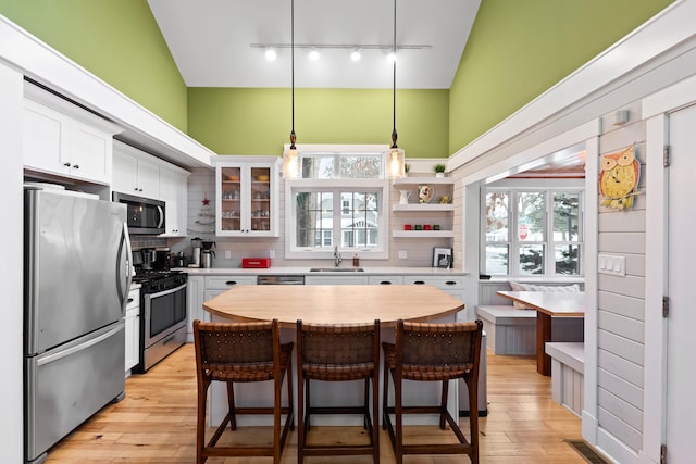 kitchen with appliances with stainless steel finishes, a kitchen island, sink, decorative light fixtures, and white cabinetry