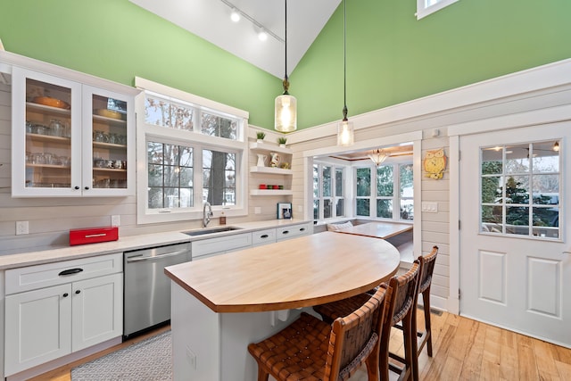 kitchen with sink, stainless steel dishwasher, decorative light fixtures, a kitchen island, and white cabinetry