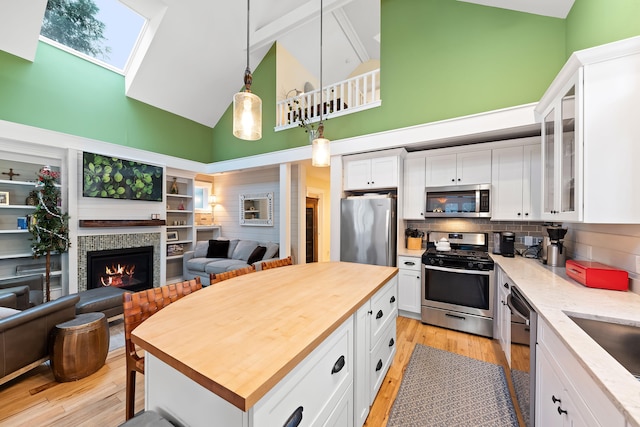 kitchen featuring white cabinetry, stainless steel appliances, high vaulted ceiling, and a skylight