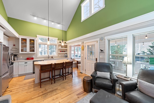 kitchen with a breakfast bar, a towering ceiling, appliances with stainless steel finishes, decorative light fixtures, and white cabinetry