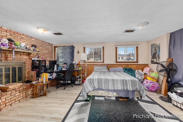 bedroom featuring wood walls, light hardwood / wood-style flooring, brick wall, and a brick fireplace