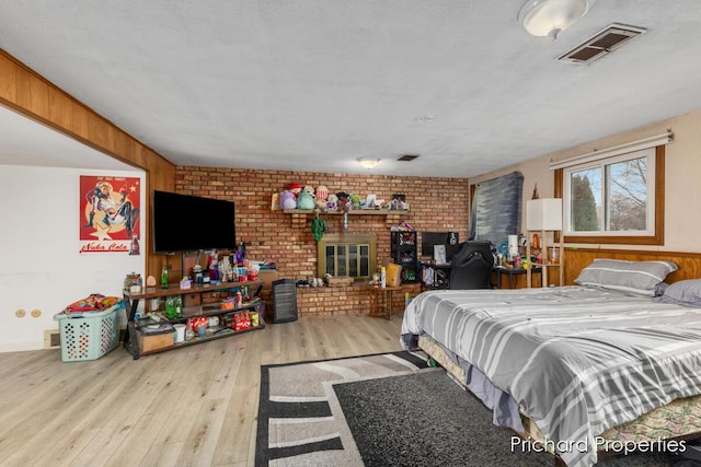 bedroom featuring wooden walls, light wood-type flooring, brick wall, and a brick fireplace