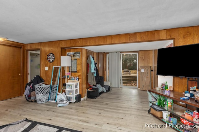 living room featuring light wood-type flooring, a textured ceiling, and wooden walls