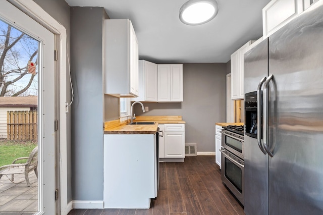 kitchen featuring butcher block counters, white cabinets, a healthy amount of sunlight, and appliances with stainless steel finishes