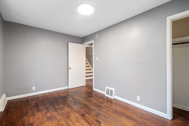 unfurnished bedroom featuring a spacious closet, dark wood-type flooring, and a closet