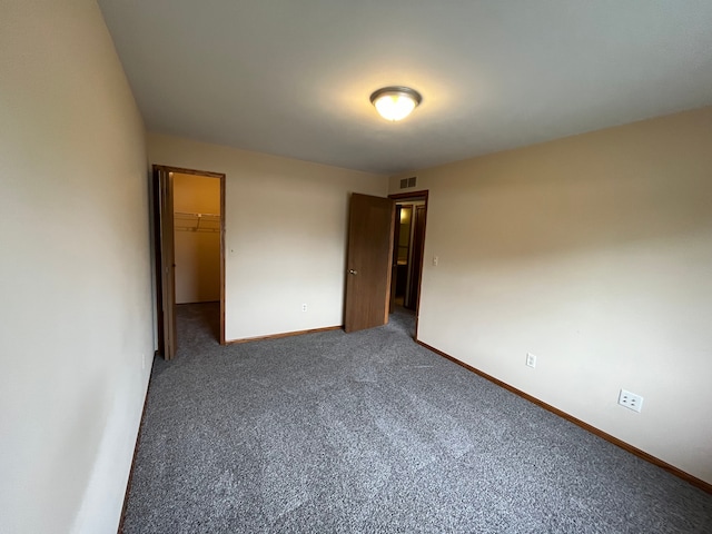 unfurnished bedroom featuring a walk in closet, a closet, and dark carpet