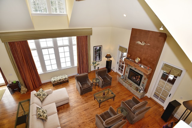 living room with light wood-style floors, baseboards, high vaulted ceiling, and a glass covered fireplace