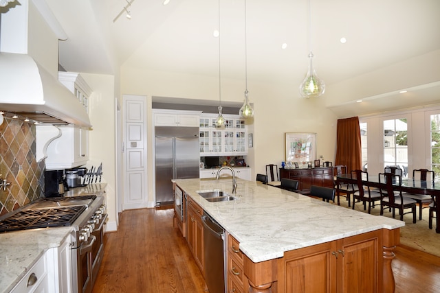 kitchen with high quality appliances, white cabinetry, ventilation hood, and a center island with sink