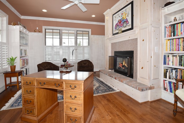 home office featuring built in shelves, a fireplace, ornamental molding, ceiling fan, and light wood-type flooring