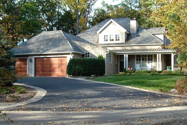 view of front of home with a garage, covered porch, driveway, stone siding, and a front yard