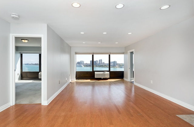 empty room featuring a wall mounted AC, light wood-type flooring, a water view, and plenty of natural light